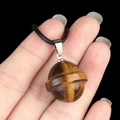 Tiger eye stone planet pendant with silver clasp and black cord shown in hand - Planet Shape (1926) / Tiger's Eye