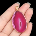 Pink agate geode slice pendant with gold-plated edges held in hand on black background - Fuchsia Agate (Gold Edge)