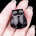 Miniature owl figurine carved from polished black obsidian stone held in hand - Obsidian