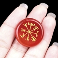 Polished red agate stone disc with golden Vegvisir viking symbol held in hand - Red Agate
