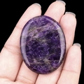 Polished purple amethyst worry stone with natural crystal texture held in hand - Amethyst