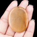 Handheld view of a polished oval yellow worry stone with natural black mineral spots - Yellow Jade