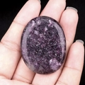 Handheld view of polished oval purple lepidolite worry stone with natural crystal texture - Lilac Stone