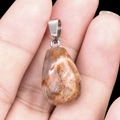 Mano sosteniendo un colgante de piedra natural de 20mm con forma de gota de agua - Jaspe Oceánico (Sola)