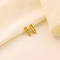 Détail macro d'un pendentif en lettre H dorée ajourée sur fond de tissu en soie - Lettre évidée H