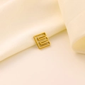 Détail macro d'un pendentif géométrique carré doré sur un tissu en soie doux - Lettre évidée E
