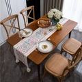 Chemin de table bohème avec motifs géométriques colorés et glands blancs sur table en bois - Petit Style / Style Géométrique Coloré