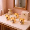 Detail of four gold hammered rings with large white pearls and crystal halo on a beige table - Adjustable Open / Amber
