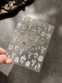 Dettaglio di adesivi per unghie 3D metallici con serpenti e ali vintage su base chiara - Luce di Conchiglia YT4297Te