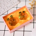 Zwei bernsteinfarbene Glasschweine in einer rosa Geschenkbox auf einem Schreibtisch - Boxed Ornament / Grün