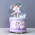 Detail of a purple musical snow globe featuring a ballerina, swans and floral relief - Automatic Snowfall + Music + Light / Ballerina Girl Purple