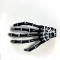 Detailed view of the metal spring clip on the back of the skeleton hand hair accessory - Black