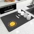 Detalle del tapete de secado negro con estampado de sol amarillo en la encimera moderna - Sol