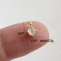 Macro shot of a 0.5cm round moonstone pendant with 18k gold plated bezel on a finger - White Round Cat's Eye Stone Pendant