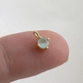 Close-up of a mini light blue zircon pendant in 18k gold plating held on a fingertip - Light Blue Round Gemstone Pendant