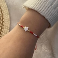 Detail of adjustable beaded bracelet featuring a shell star charm and red cord on wrist - Red