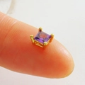 Vue macro d'une perle carrée en zircon violet doré tenue entre les doigts - Strass Carré Violet-Or (21)