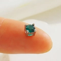Macro shot of a tiny green round-cut gemstone in a four-claw silver setting on a fingertip - Green Round Rhinestone-Silver (04)
