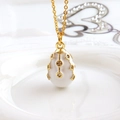 Macro detail of white enamel egg pendant with gold cross lines and sparkling crystals - White