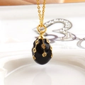 Macro view of a black enamel egg pendant with gold geometric lines and crystals - Black