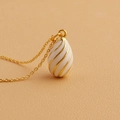 Macro shot of egg-shaped enamel pendant with golden spiral details on leather background - White
