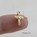 Detailaufnahme eines kleinen goldenen Kreuzanhängers mit strukturierter Oberfläche am Finger - Gold(01)