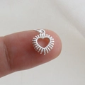 Vista macro di un piccolo ciondolo a cuore argentato con raggi solari sulla punta del dito - Stile Mini Radiale Cuore Argento (26)