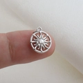 Close-up of a silver sunburst charm pendant held by hand to show 12mm scale and detail - Silver Rotating Radiant Sun Star Style (02)
