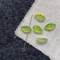 Macro shot of green glass leaf beads with iridescent gold coating and detailed vein texture - Green Leaf