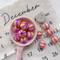 Detailed shot of striped colorful resin beads on a pink spoon for DIY craft projects - Style 7 Purple Yellow Striped 12mm