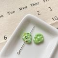 Vue macro de perles nuages vert pastel avec un smiley et un charme de palette de peintre - Biscuit Souriant Vert
