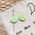 Detail of light green fish-shaped enamel charm and silver pin on rustic burlap background - Green Dried Fish