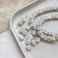 Macro detail of white cubic Czech glass beads with golden sun pattern and vintage finish - Rounded Cube (1#) / Grayish White