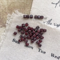 Macro view of square Picasso finish Czech glass beads with red marble texture on linen - Size 8