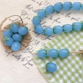 Macro shot of blueberry-shaped sky blue lampwork glass beads with green leaf details - Blue