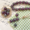 Macro detail of purple glass eggplant beads with green leaf accents for DIY jewelry making - Deep Purple