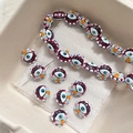 Macro view of colorful evil eye glass beads and a beading needle for DIY jewelry making - Dark Red