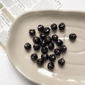 Detailed view of black pumpkin-shaped glass beads with gold accents on a ceramic tray - 1 Piece / 16# Glossy Black