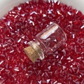 Makroaufnahme einer kleinen Glasflasche mit Korken auf roten dreieckigen Kristallperlen - Rot