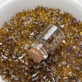 Makroaufnahme von gold-lila Glas-Strasssteinen mit einer kleinen Glasflasche für DIY - Erzgold