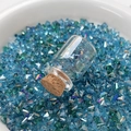 Makroaufnahme einer Glasampulle mit Korken inmitten funkelnder meeresblauer Kristalle - Blau