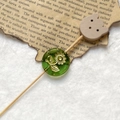 Macro detail of a green Czech glass bead with gold floral engraving on vintage paper - Light Green Gold Sunflower With Wood Bear Head (Style 15)