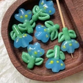 Macro detail of handmade light blue flower glass beads with green leaves on wood - 1 Piece / Blue