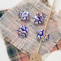 Detailed view of hand-painted ceramic fish beads for DIY jewelry on textured fabric - 11# (White Blue Orange Waves)