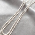 Macro shot of 4mm white shell pearls on grey satin for DIY jewelry making - 4mm