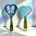 Detail of heart-shaped air cushion combs with blue holographic bow design and metallic finish - Holographic Bow Design (C)