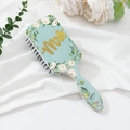 Close-up of floral air cushion hairbrush with gold Mrs lettering on light blue surface - Customizable Pattern / Gold White Clover