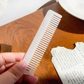 Handheld wide-tooth ivory white acetate hair comb for curly hair on a wooden background - Mermaid White
