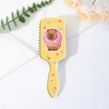 Close-up of yellow hairbrush back featuring a cute capybara print and hanging handle - Donut Capybara Style (C)