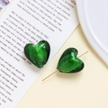 Dettaglio di orecchini a cuore in vetro verde con perni dorati su una rivista - verde scuro